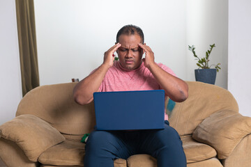 A man is sitting on a couch with a laptop in front of him
