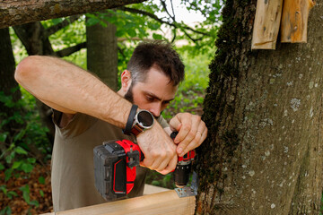 brutal young brunette man, dad with beard is nailing building a tree house to his little son with...