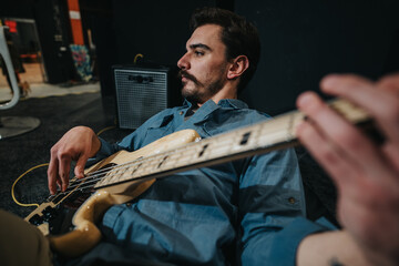 Young man playing an electric bass guitar, lying down in a relaxed position within a music studio...