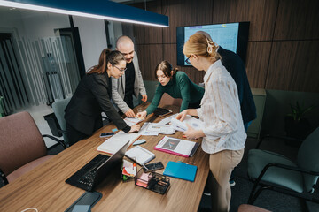 Diverse team of employees collaborating on a project in a contemporary office setting with documents, a laptop, and a presentation.