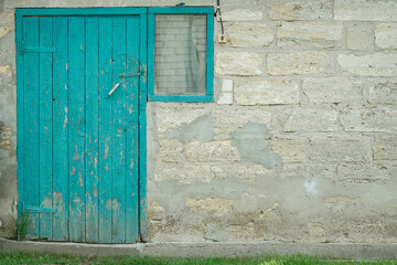 Weathered turquoise door and window on an old stone wall, with green grass in the foreground.