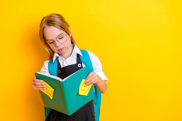 Young schoolgirl studying with a book wearing a uniform and glasses against a bright yellow...