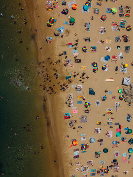 Aerial drone top down view of a crowded beach with colorful umbrellas and sunbathers during a summer afternoon near the coast