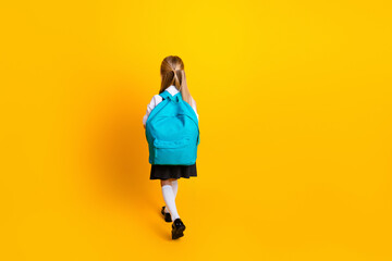 Young schoolgirl with a blue backpack standing on a vibrant yellow background, symbolizing...