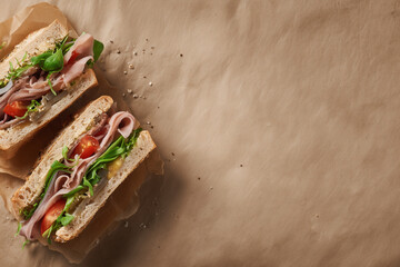 Flat lay of a gourmet sandwich cut in half, ingredients visible and neatly arranged, placed on parchment paper