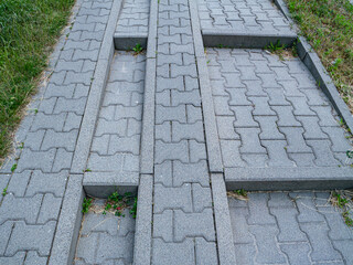 Concrete sidewalk ramp with two parallel grooves, likely designed for wheel access. Made of...