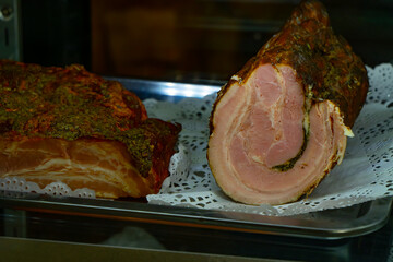 Close-up of traditional rolled ham and herb-crusted smoked bacon in a delicatessen display, served...