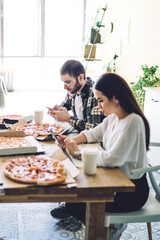 Fellows speaking and surfing smartphones at table with pizza in canteen