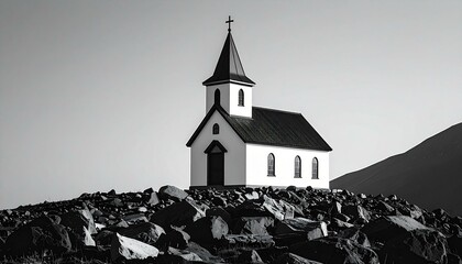 Black and white photo of a small church situated on a rocky hill against a mountain backdrop