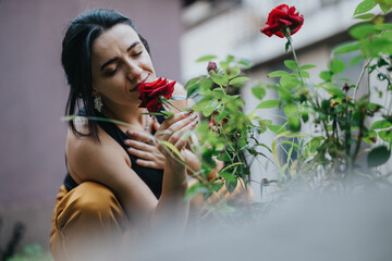 A young woman with a peaceful expression inhales the fragrance of vibrant red roses in a garden.