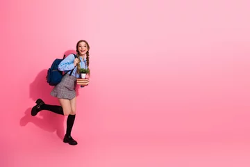 Fototapete Happy female student holding a plant and boo book s while posing cheerfully against a vibrant pink background © deagreez