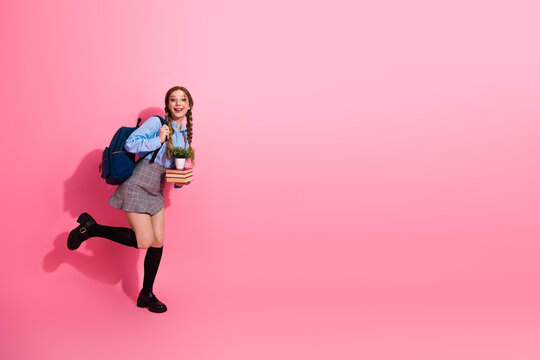 Happy female student holding a plant and boo book s while posing cheerfully against a vibrant pink background
