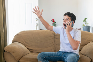A boy is sitting on a couch and talking on a cell phone