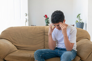 A young man sits on a couch with his head in his hands