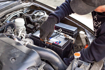A man wearing gloves disconnects a battery terminal by loosening the clamp. Replacing a battery on a car