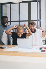 Group of enthusiastic multiethnic coworkers using laptop at office