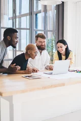 Gordijnen Group of concentrated multiethnic coworkers using laptop at office © BullRun