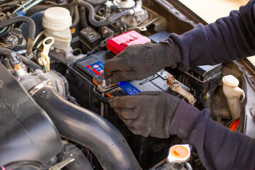 A man wearing gloves securely fastens a car battery terminal after installing it under the hood. Replacing a weak battery