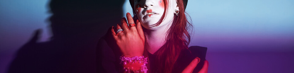 Caucasian teenage girl with creative face paint and jewelry posing with hand near face, looking...
