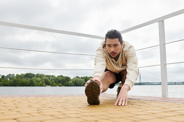 Sporty man stretching outdoors during early morning workout along the riverbank