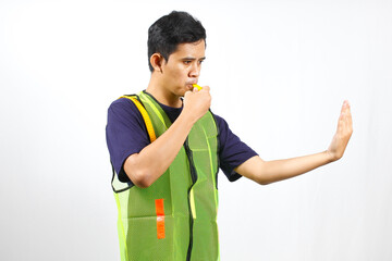 Asian parking attendant wearing green vest blowing whistle while giving stop sign