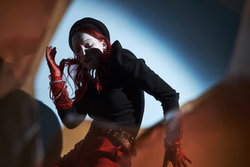 Caucasian teenager girl with red hair wearing mime makeup performing expressive gesture at home,...