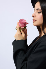 A stylish brunette woman in a wide-brimmed black hat poses against a light background holding...
