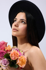 A stylish brunette woman in a wide-brimmed black hat poses against a light background holding...