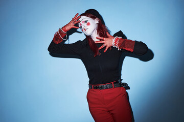 Caucasian teenager girl with creative makeup and red gloves performing expressive mime gesture...
