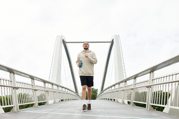 Sporty young man jogging on a bridge while enjoying the outdoors in a hoodie