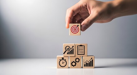 Hand placing wooden cube with target arrow on top of stacked cubes showing graphs checklist stopwatch and gears