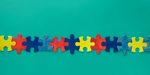 Autism awareness Day, colorful puzzle pieces arranged in a straight line on a vibrant green...