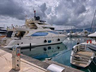 Luxury yacht docked at marina in Porto Montenegro with cloudy sky and calm water reflections