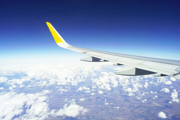 Flying in good weather: airplane wing above the clouds. Aerial view from cabin window with white...