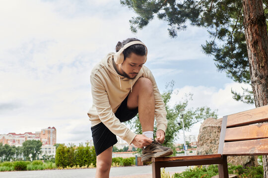 Young sporty man in hoodie ties shoelaces before outdoor workout session