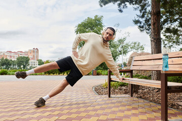 Dedicated young man in hoodie engages in outdoor workout routine by park bench