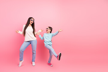 Joyful mom and daughter dancing in vibrant casual outfits against a cheerful pink backdrop