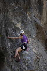 A woman is climbing a rock wall wearing a purple shirt and black shorts