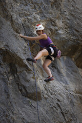 A woman is climbing a rock wall with a blue rope