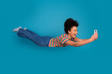 Joyful young woman with curly hairstyle taking a selfie in mid-air while wearing vibrant striped...