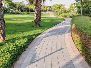 Small Interlock Path Between Landscaping Area.
Green And Lush Landscaping Area With Carpet Grass And Trees Like Palm Or Washingtonia, Some Houses Or Villa's Also Beside Gardens Padestrian Pathway.
