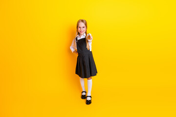 Happy schoolgirl in uniform posing on yellow background showing positive gestures and ready for...