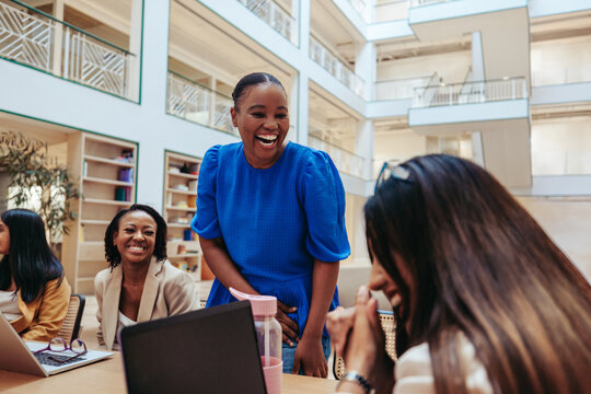 Joyful business team meeting with diverse coworkers laughing and engaging in a friendly conversation around a table