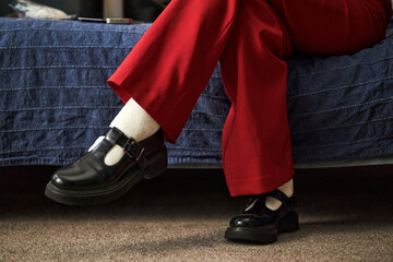 Caucasian teenager girl sitting on bed with legs crossed, wearing black shoes and socks, creative...