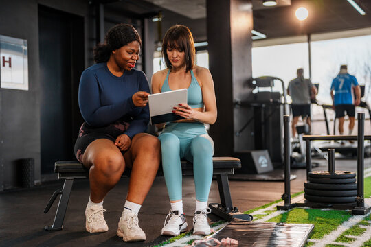 Overweight woman consults with her personal trainer, reviewing a training plan on a tablet in a modern gym, demonstrating their commitment to fitness and a healthy lifestyle