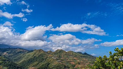A breathtaking view of green hills and terraced farmland beneath a vibrant blue sky filled with fluffy white clouds, showcasing nature's harmony and rural beauty.