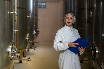 Female wine enologist inspecting modern stainless steel barrel fermentation for quality control in wine factory production