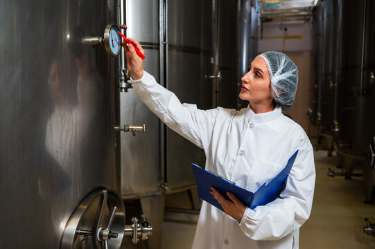 Female wine enologist inspecting modern stainless steel barrel fermentation for quality control in wine factory production