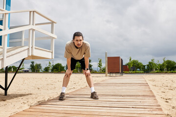 Fit young man takes a break from outdoor workout on a cloudy day by the beach