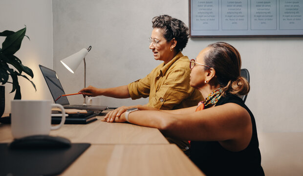 Two women collaborating on a project at an office desk - Powered by Adobe